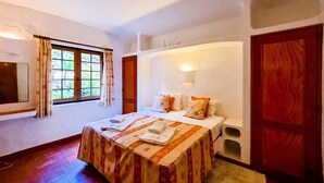 Ein Schlafzimmer mit einem Bett, einem Fenster mit Vorhängen, einem Nachttisch und einer Wandleuchte.