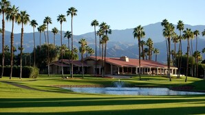 A golf course with a clubhouse, palm trees, and mountains in the background. - Winter Escape in Chaparral Country Club (Palm Desert)