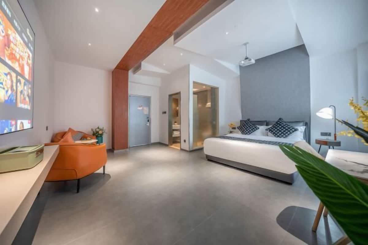 A modern bedroom with a bed, a desk, and a chair. There is a door leading to another room.