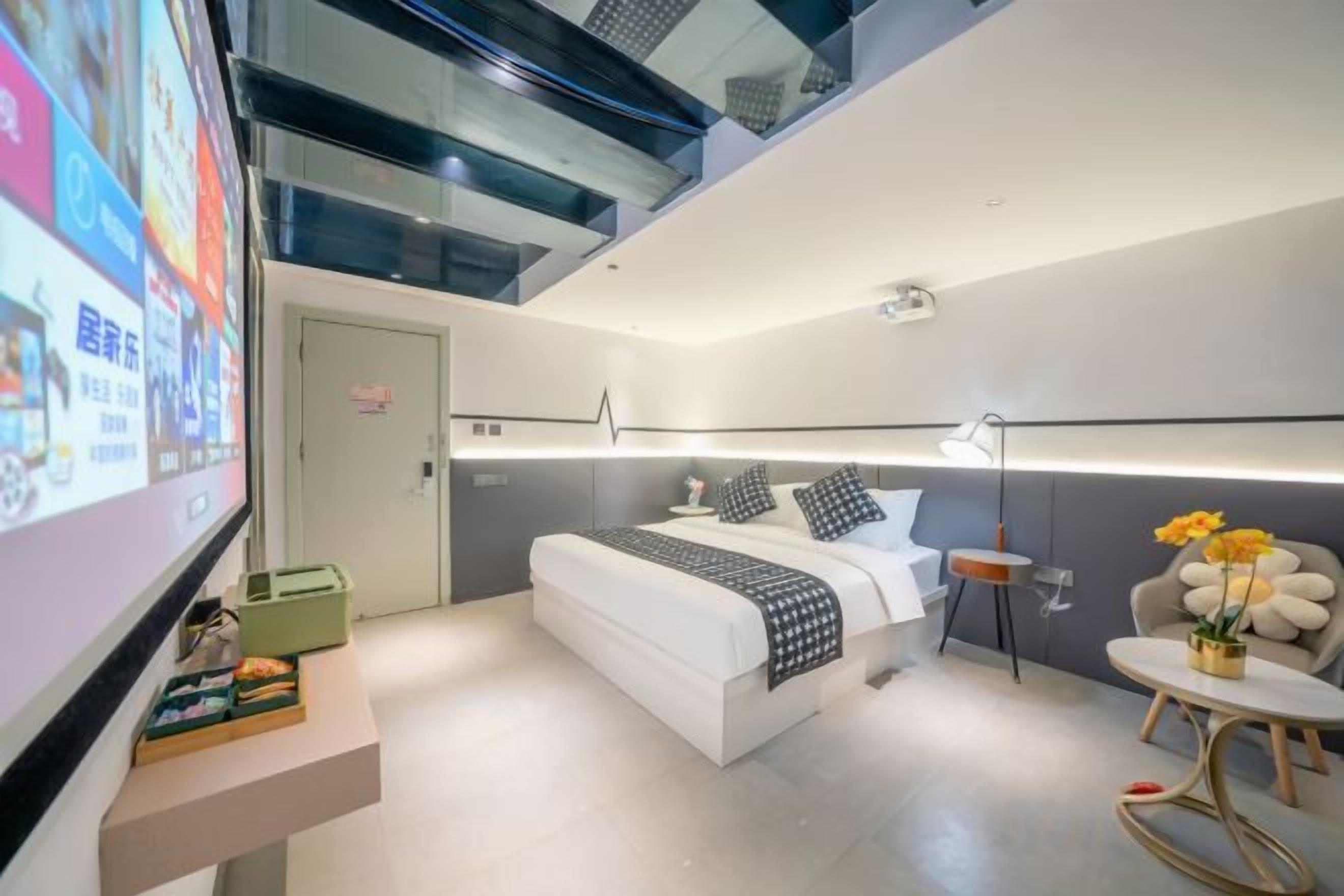 A modern hotel room with a bed, bedside table, and a small round table with flowers.