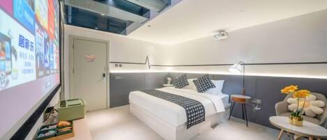 A modern hotel room with a bed, bedside table, and a small round table with flowers.