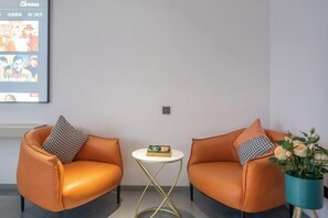 Two orange leather sofas with checkered pillows, a small round table with a book, and a potted plant with white flowers. - Zhiling Homestay (Five Star Street City Center) (Liuzhou)