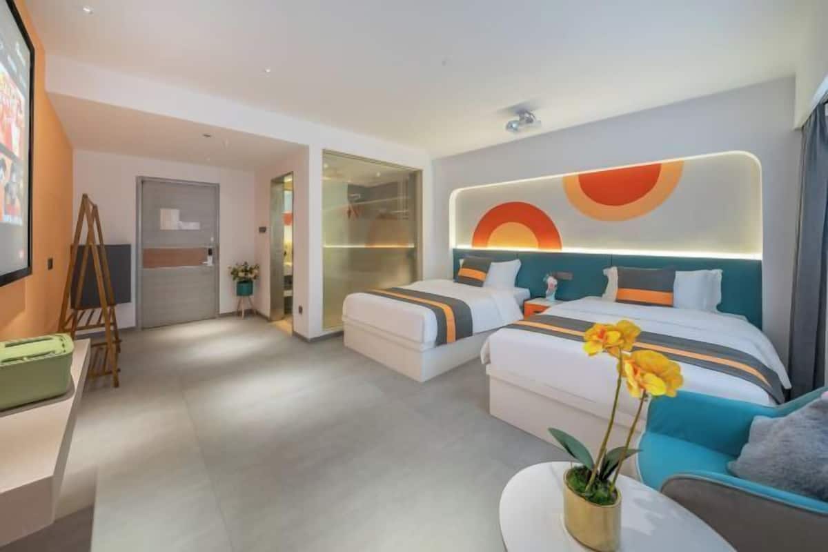 A modern hotel room with a large bed, a smaller bed, a desk, and a seating area with a plant.