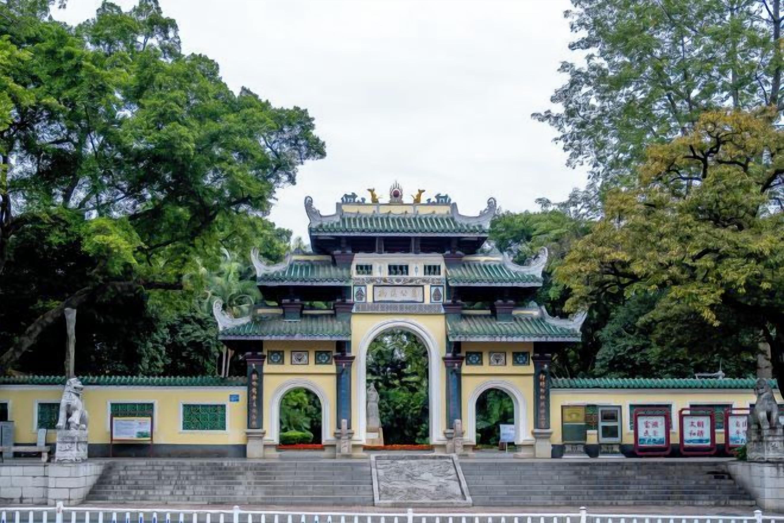 A traditional Chinese gate with a multi-tiered roof, surrounded by trees and a paved walkway.