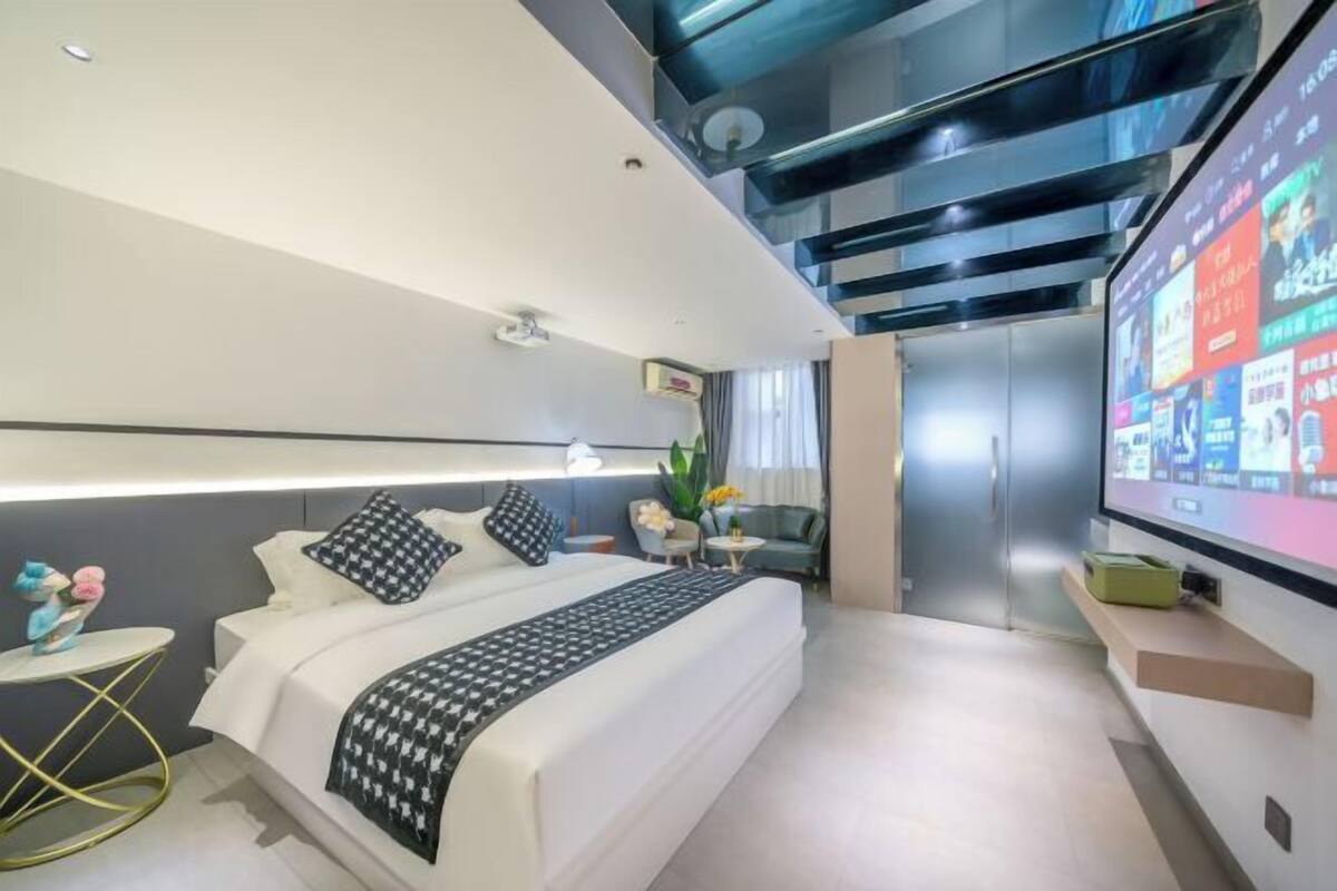 A modern hotel room with a large bed, a TV, a small table, and a sofa.