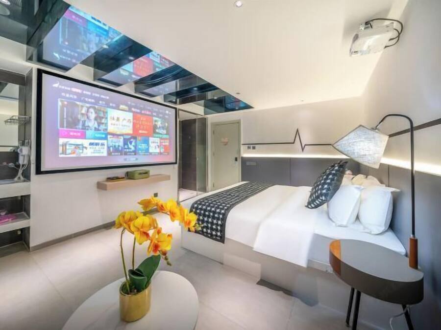 Et moderne hotelværelse med en stor seng, et natbord, et skrivebord og et fjernsyn, der viser et digitalt interface.