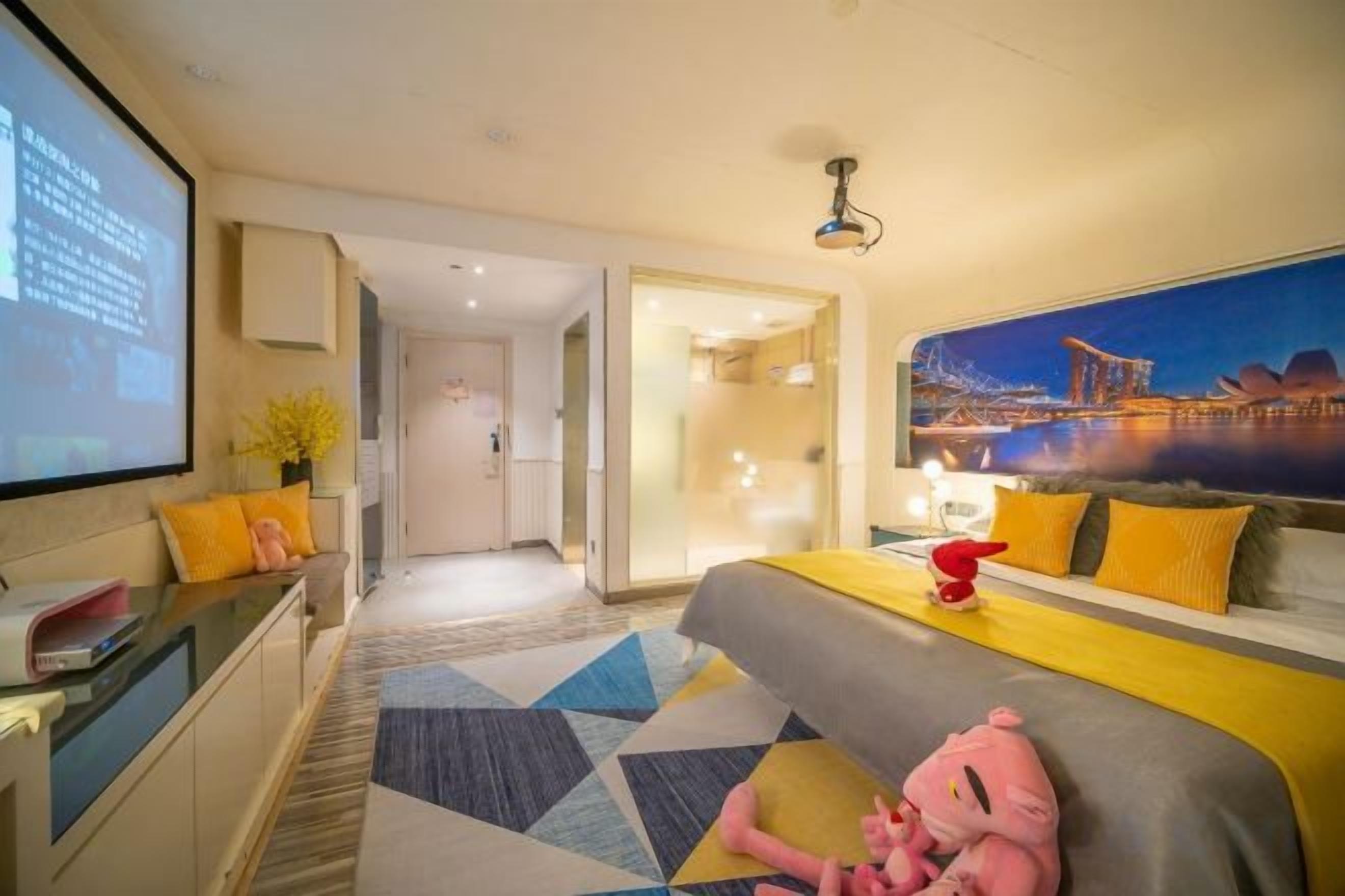 Habitación de hotel con cama, escritorio, pantalla de proyector y ventana grande con vista a la ciudad.