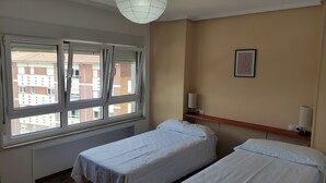 A room with two single beds, a window with blinds, a wall-mounted shelf with a lamp, and a framed picture. - Spacious and bright apartment near the beach..!! (Piedras Blancas)