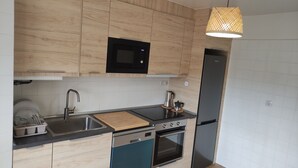A modern kitchen with wooden cabinetry, a black microwave, stainless steel sink, and a built-in oven. - Spacious and bright apartment near the beach..!! (Piedras Blancas)