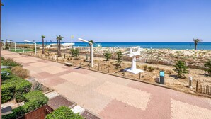 Un paseo marítimo frente a la playa, con vista despejada al mar, palmeras y una zona de arena.