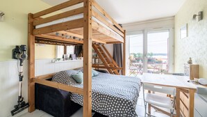 A room with a wooden bunk bed, a desk with a chair, and a window with a view of the outside. - L'Effet Mer - Studio Apartment, Sleeps 4 (La Richardais)
