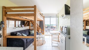 A cozy living area with a bunk bed, a sofa, a dining table, and a kitchen area. - L'Effet Mer - Studio Apartment, Sleeps 4 (La Richardais)