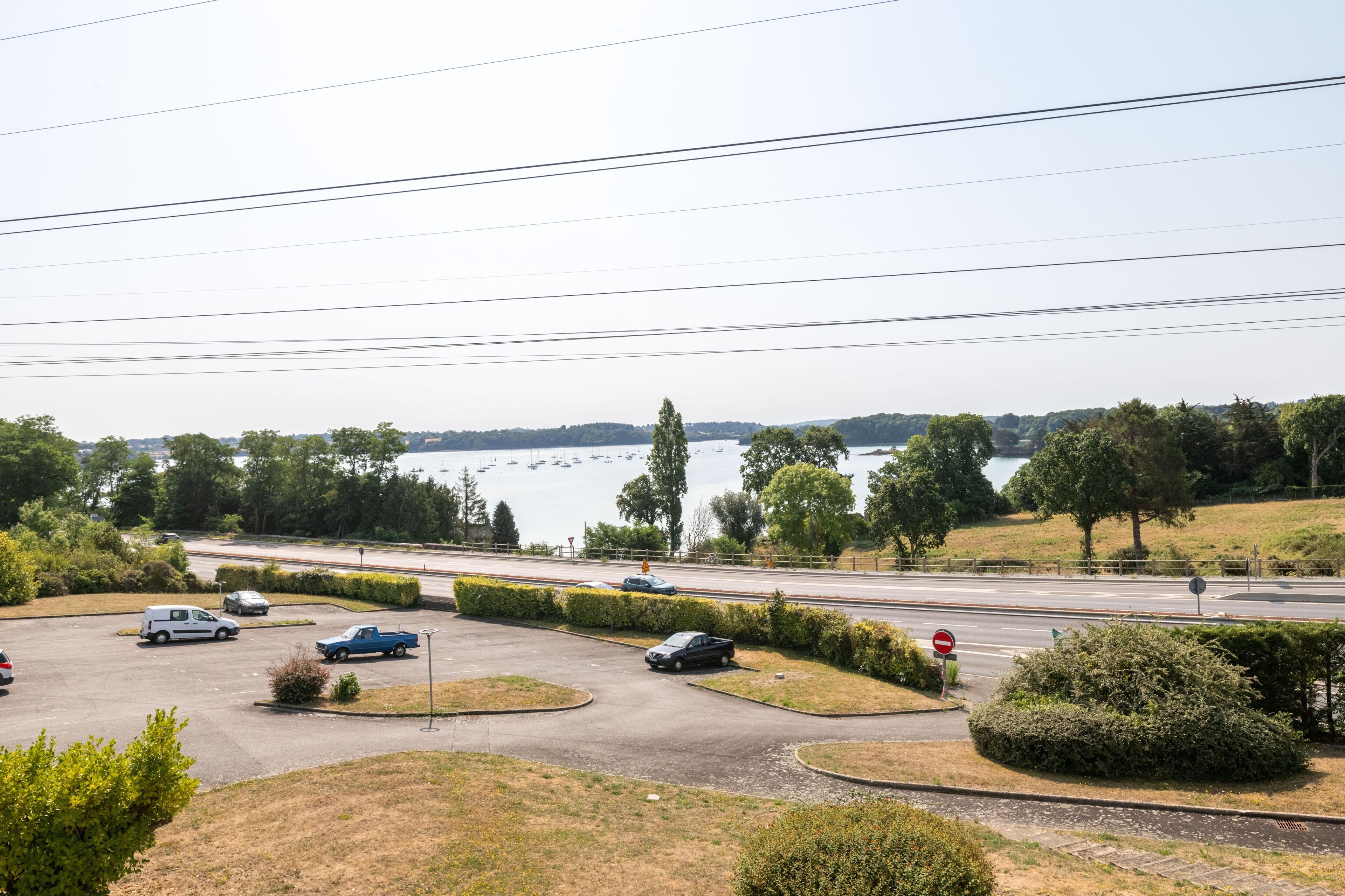 A parking lot with several cars, a road with a 'no entry' sign, and a body of water in the background.