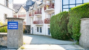 A residential building with multiple balconies, a stone pillar with a sign, and a well-maintained hedge. - L'Effet Mer - Studio Apartment, Sleeps 4 (La Richardais)