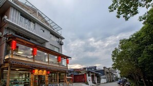 Straßenansicht mit einem traditionellen Gebäude, das eine Holzfassade und rote Laternen aufweist, einem modernen Gebäude mit einem Balkon sowie abgestellten Motorrädern.