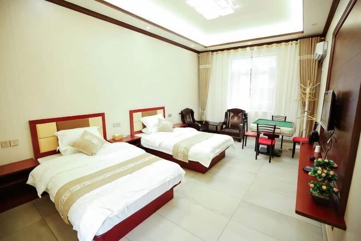 A hotel room with two beds, a desk, chairs, a TV, and a window with curtains.