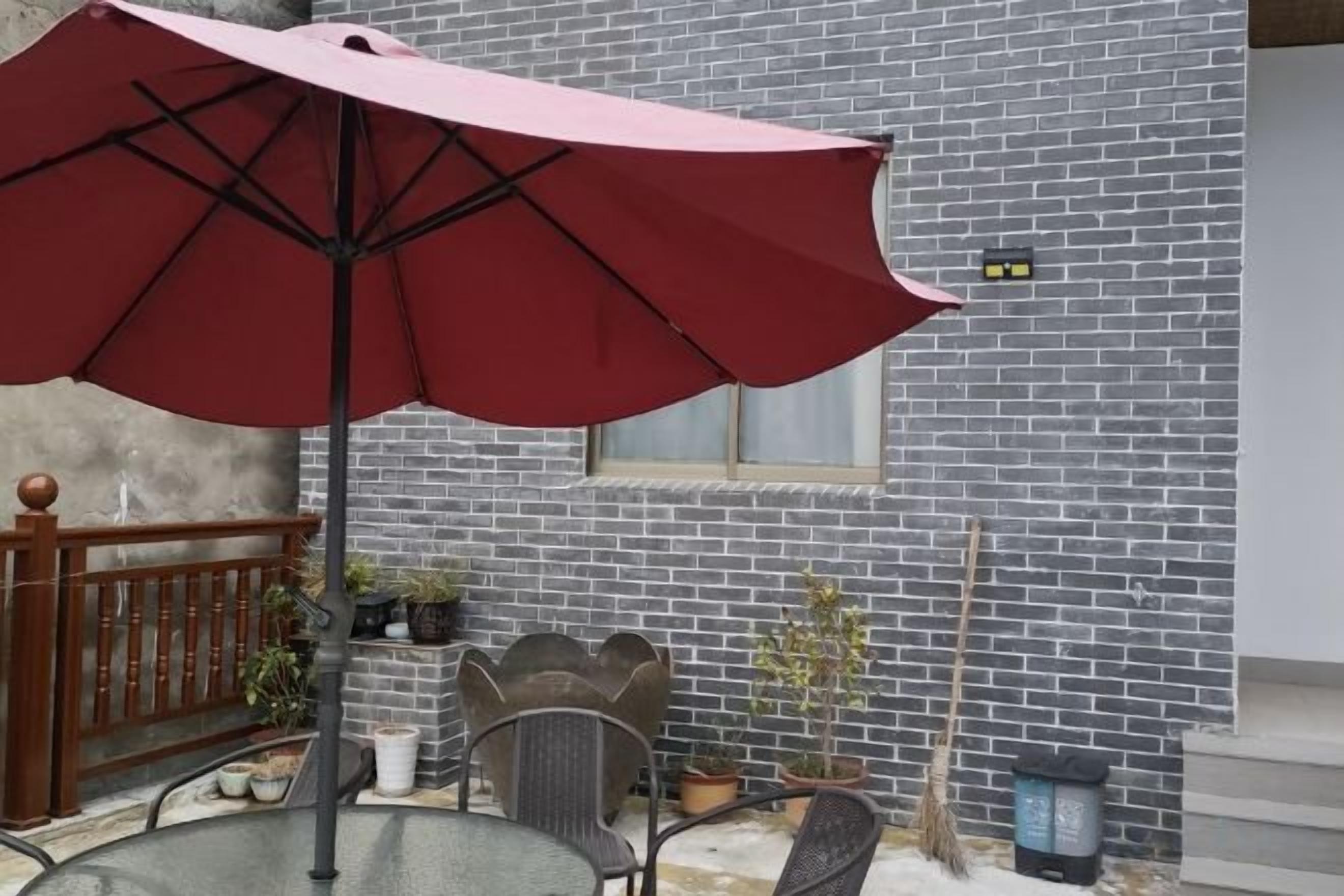 An outdoor patio with a red umbrella, metal chairs, and potted plants.