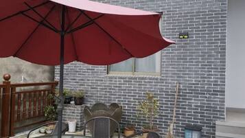 An outdoor patio with a red umbrella, metal chairs, and potted plants.