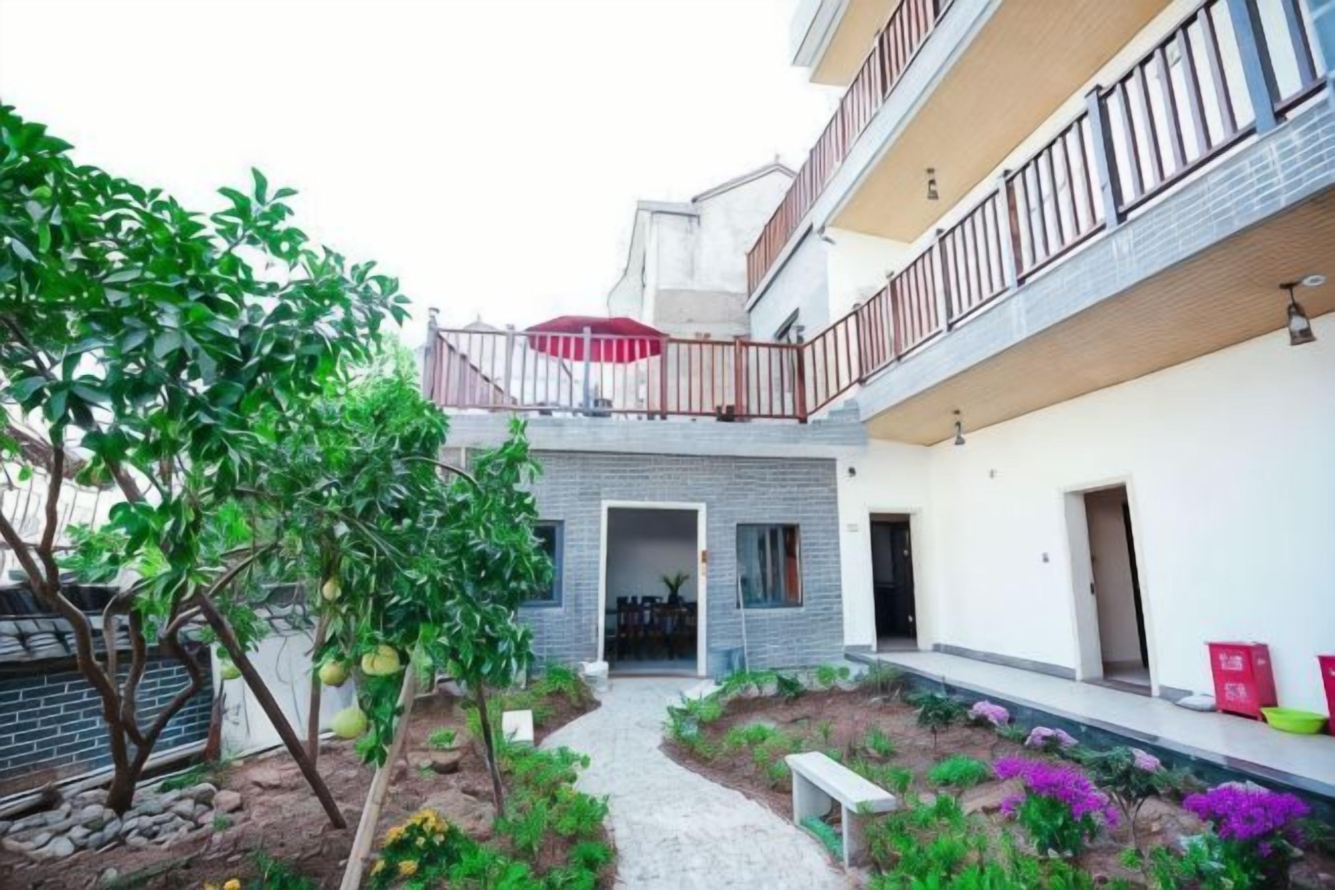 A residential building with a covered outdoor area, a pathway, and a small garden with plants and a bench.