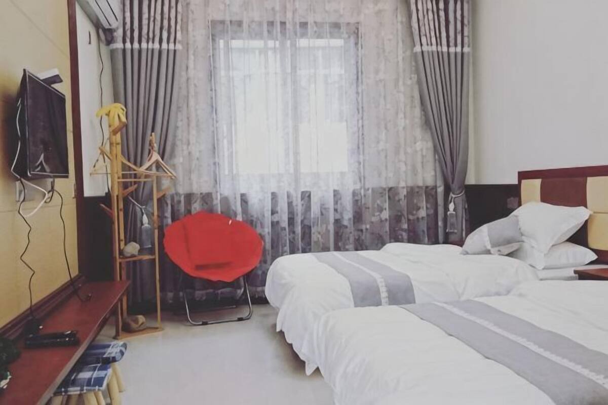 A hotel room with two beds, a TV, a red chair, and a window with curtains.