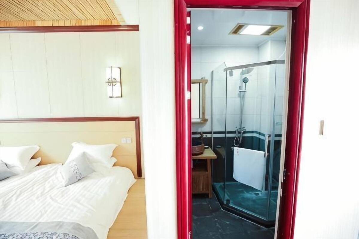 A hotel room with a bed, a desk, and a shower area.