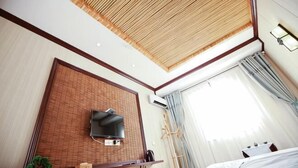 A hotel room with a television mounted on a brick wall, a ceiling fan, and a large window with curtains. - Yuyun Hostel (Tiantai County)