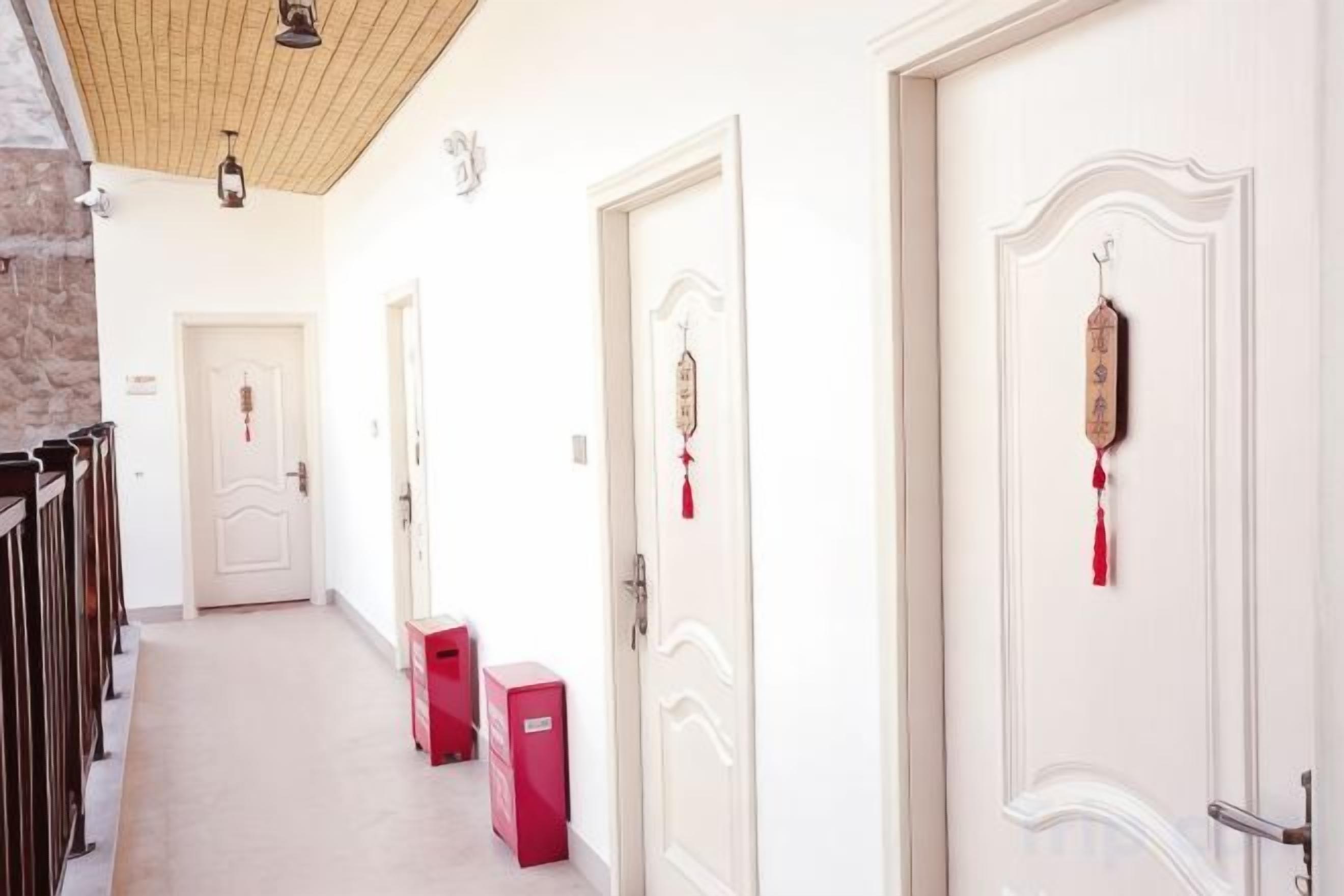 Un pasillo con puertas blancas, algunas decoradas, y una pared de piedra en un lado.
