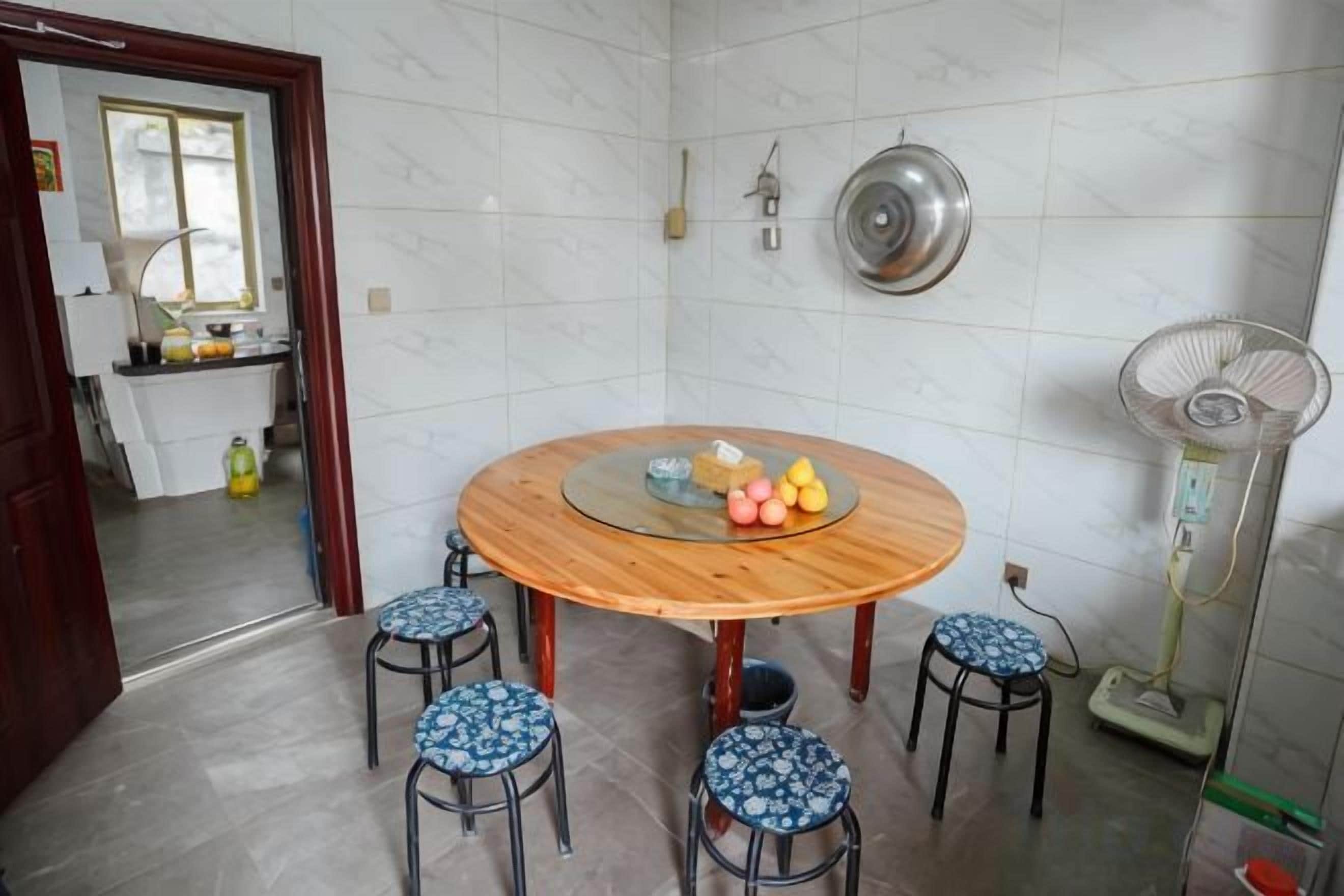 A dining area with a round wooden table, four stools, and a wall-mounted fan.