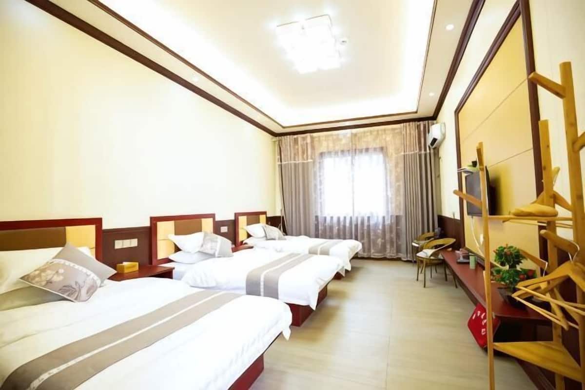 A hotel room with four beds, a desk, a chair, and a TV.