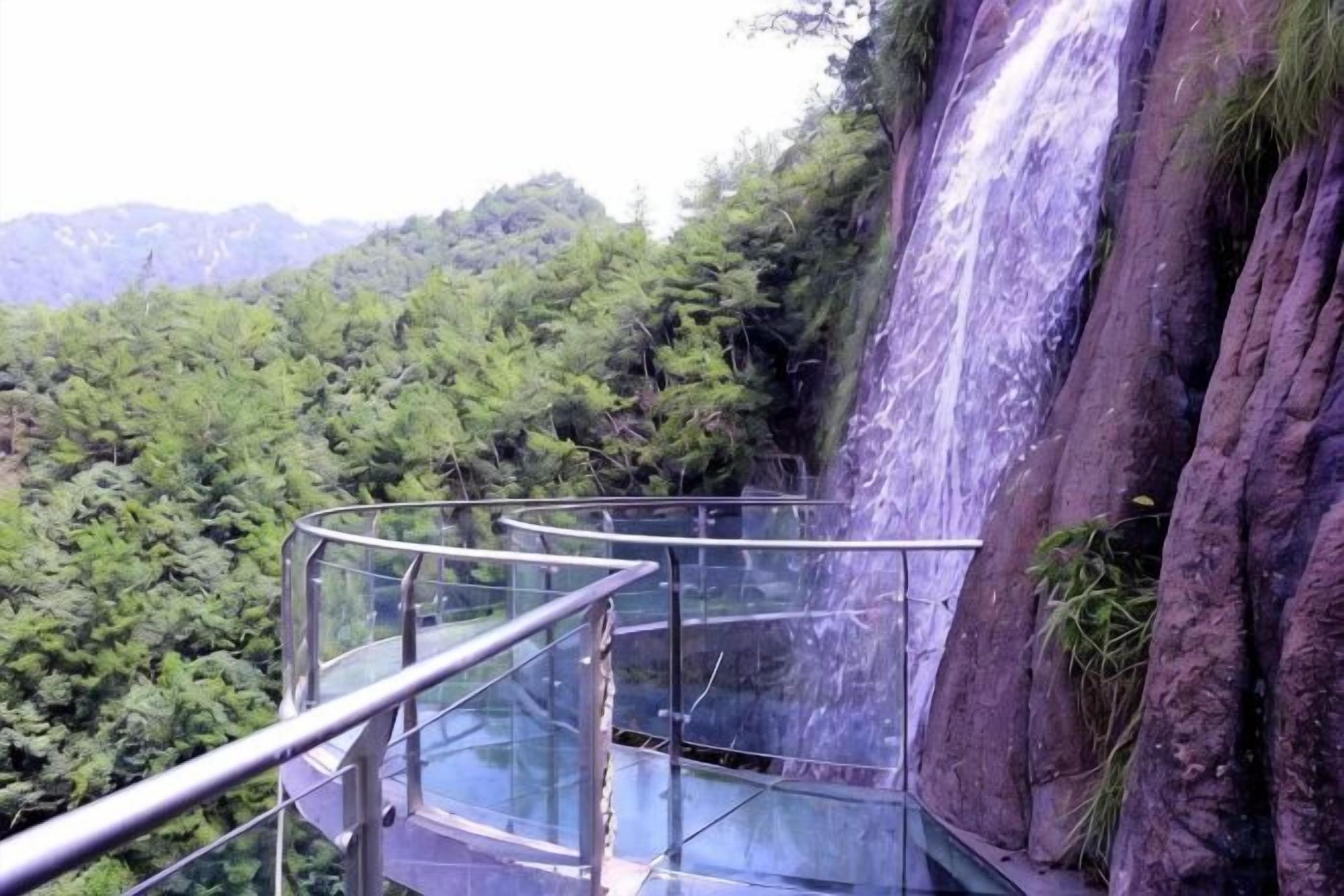 Un pasillo de vidrio con baranda metálica que da a una cascada.