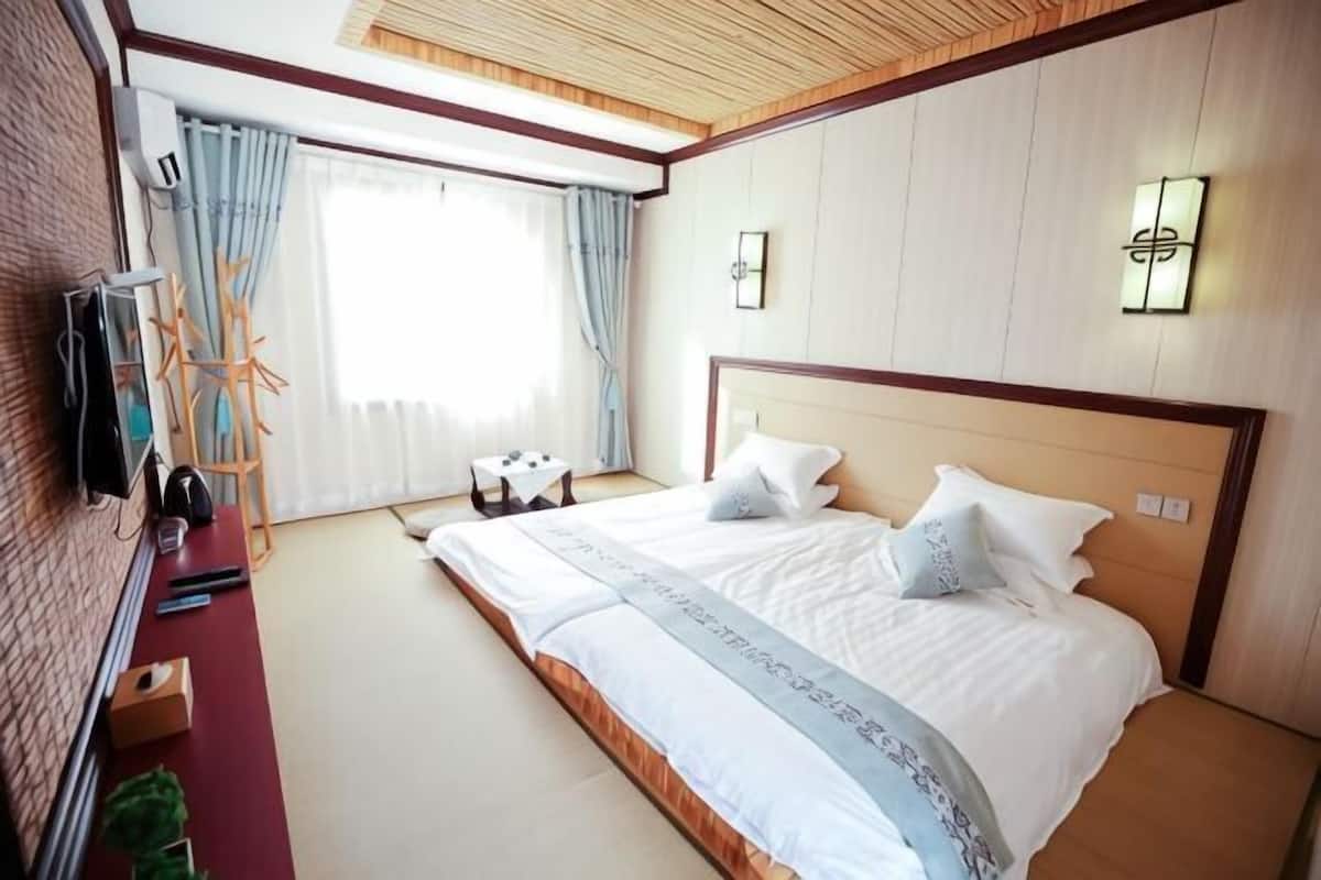 A hotel room with a large bed, a TV, a desk, and a window with curtains.