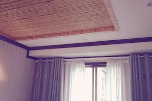 Une pièce avec un plafond en pente, une grande fenêtre avec des rideaux et une bouche d’aération visible au plafond.