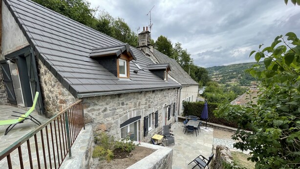 Une maison en pierre avec un toit en pente, un espace extérieur aménagé pour s’asseoir et une vue sur le paysage environnant.