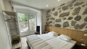 Une chambre avec un grand lit, une tête de lit en bois, un mur en pierre et une fenêtre donnant sur un paysage verdoyant.