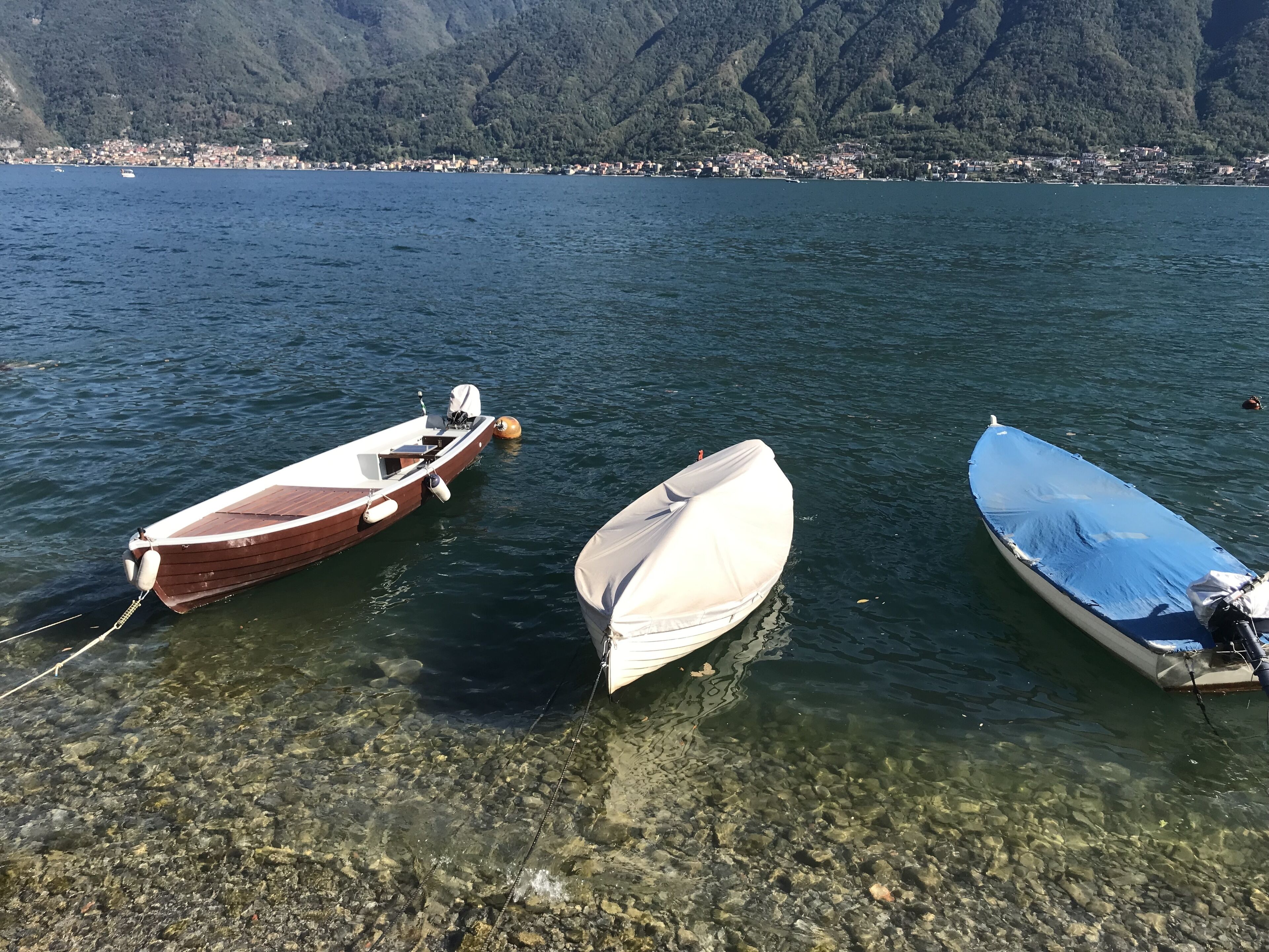 Three boats tied to a rocky shore with a mountainous backdrop.