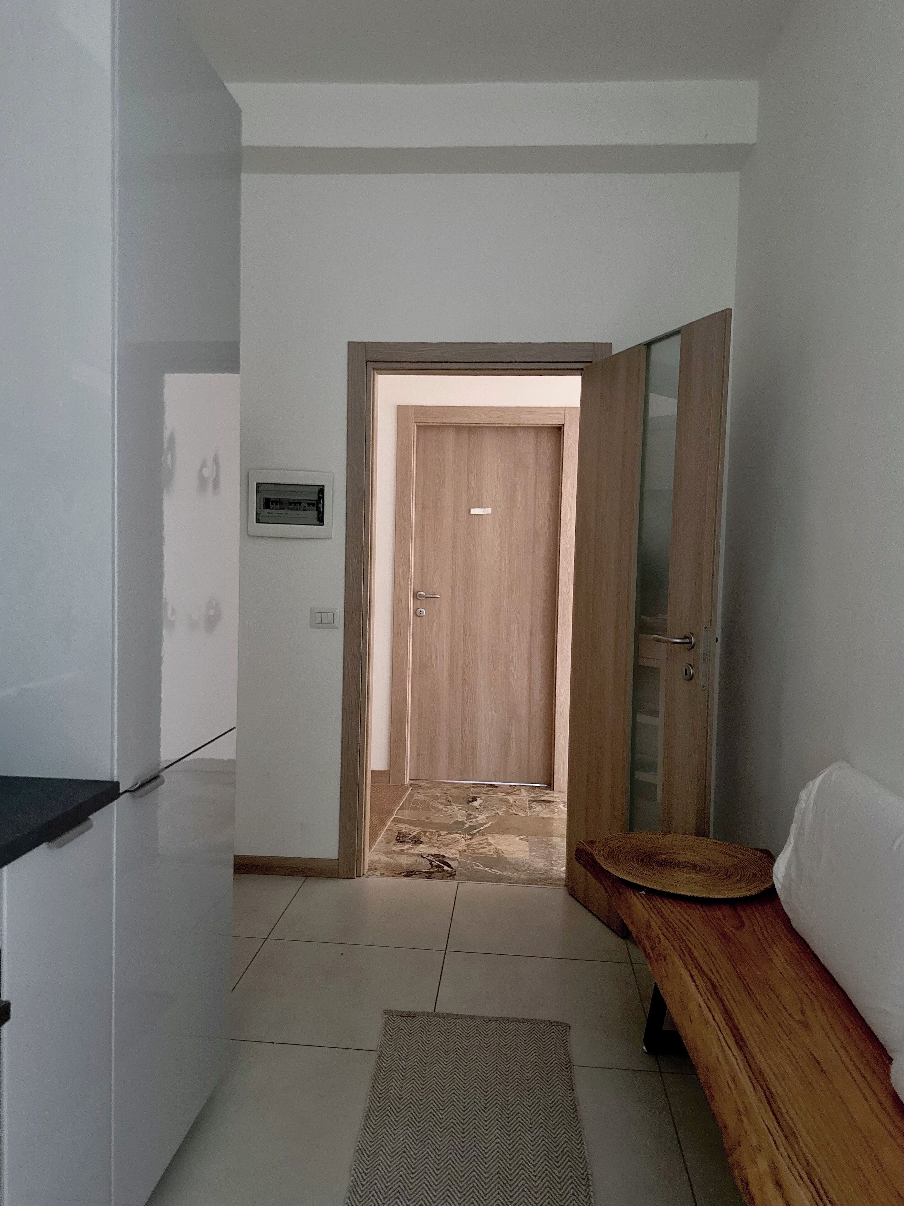 A hallway with a wooden door, a bench, and a tiled floor.