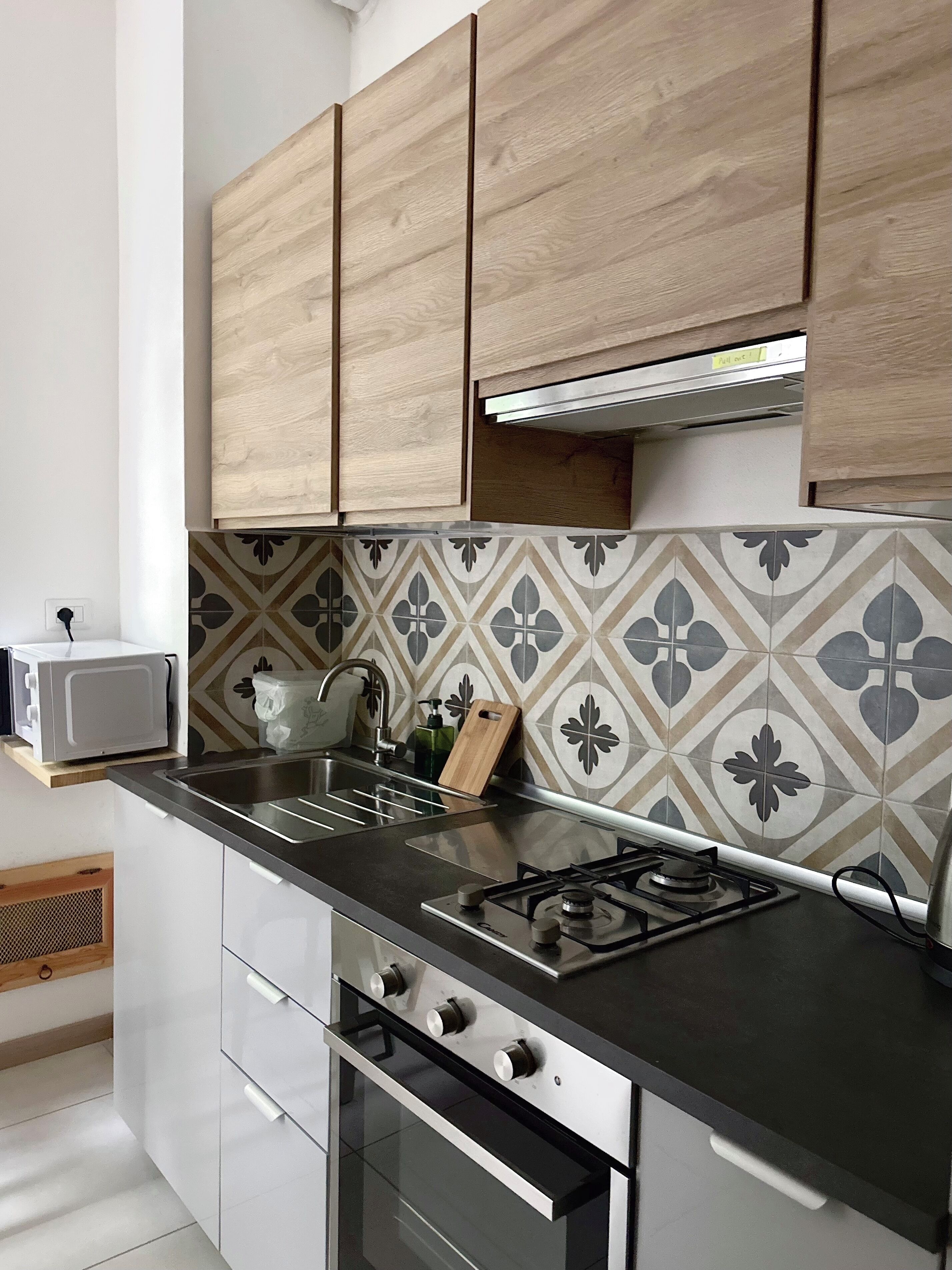 Una cucina moderna con mobili in legno, piano cottura a gas, forno a microonde e piastrelle decorative per la parete.