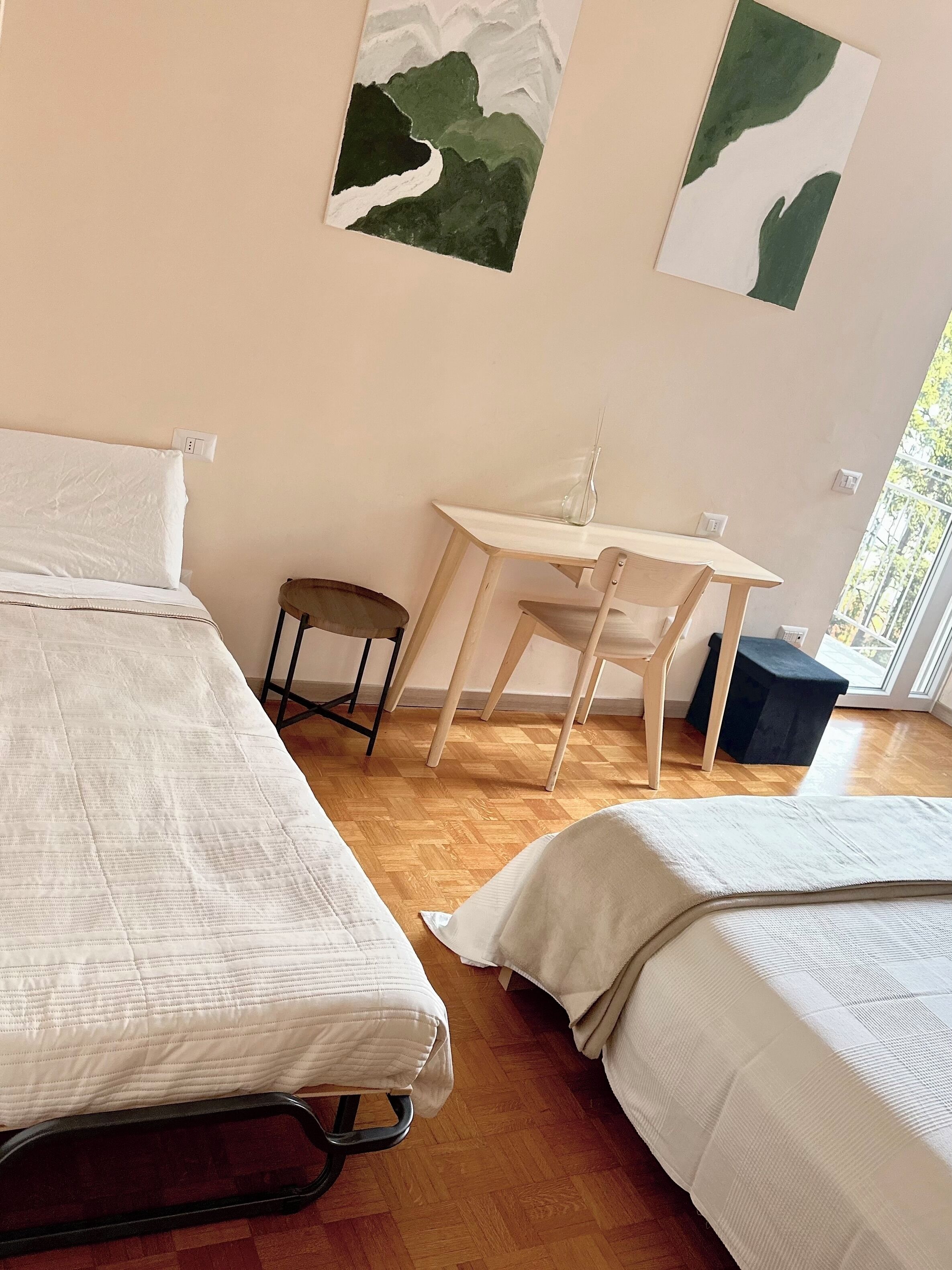 A room with two beds, a small table, and a chair. There are two paintings on the wall.