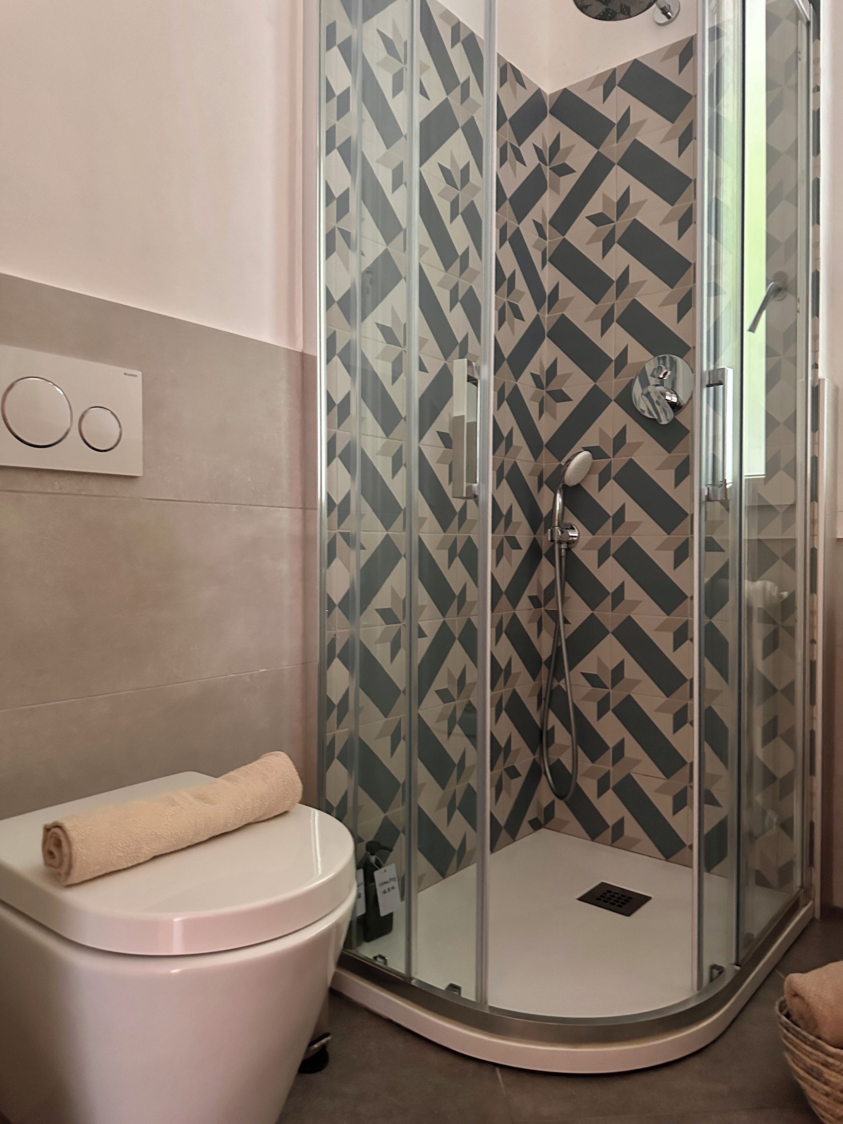 A modern bathroom with a glass shower enclosure, a toilet, and a towel on the toilet.