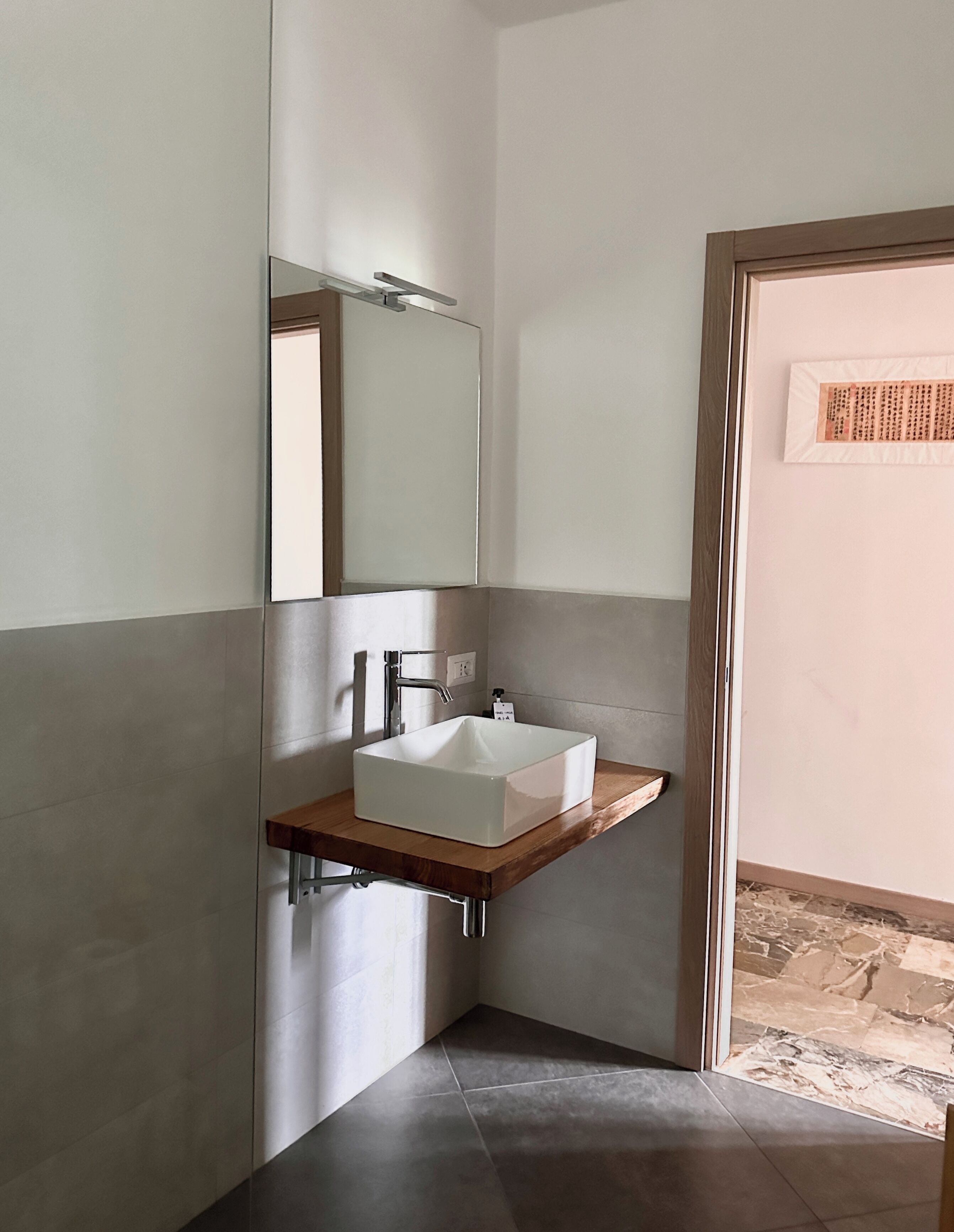 A modern bathroom with a rectangular sink, a mirror, and a wooden shelf.