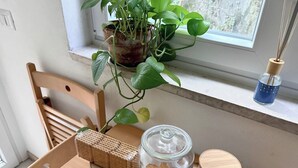 A wooden table with a glass jar, a wooden cutting board, a plant, and a small blue container on a windowsill.