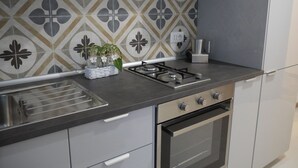 A modern kitchen with a gas stove, oven, and stainless steel sink. There is a decorative backsplash and a small plant on the counter.