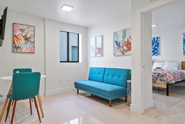 A modern living room with a blue sofa, teal chairs, and artwork on the walls.
