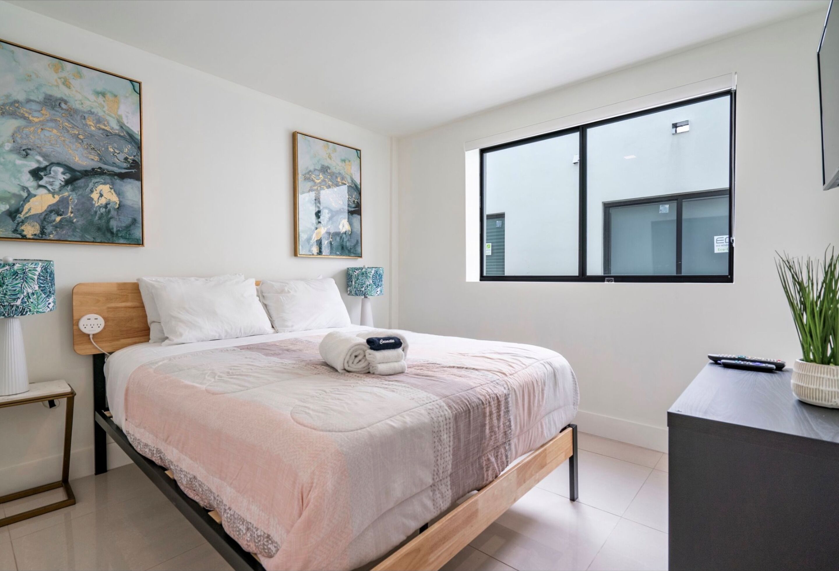 A modern bedroom with a bed, bedside tables, a desk, and a large window.