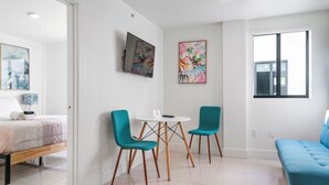 A modern, well-lit room with a bed, a small table with chairs, and artwork on the walls. - Miami Suite 303 (Miami)