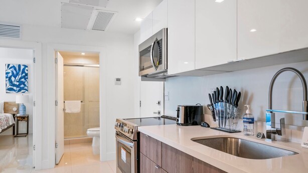 A modern kitchen with white cabinets, a stainless steel sink, and a built-in oven. - Miami Suite 303 (Miami)