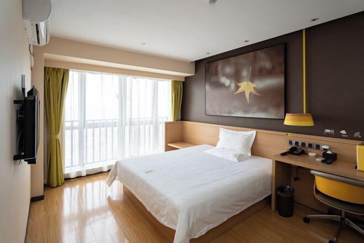A hotel room with a large bed, a desk with a chair, a TV, and a window with curtains.