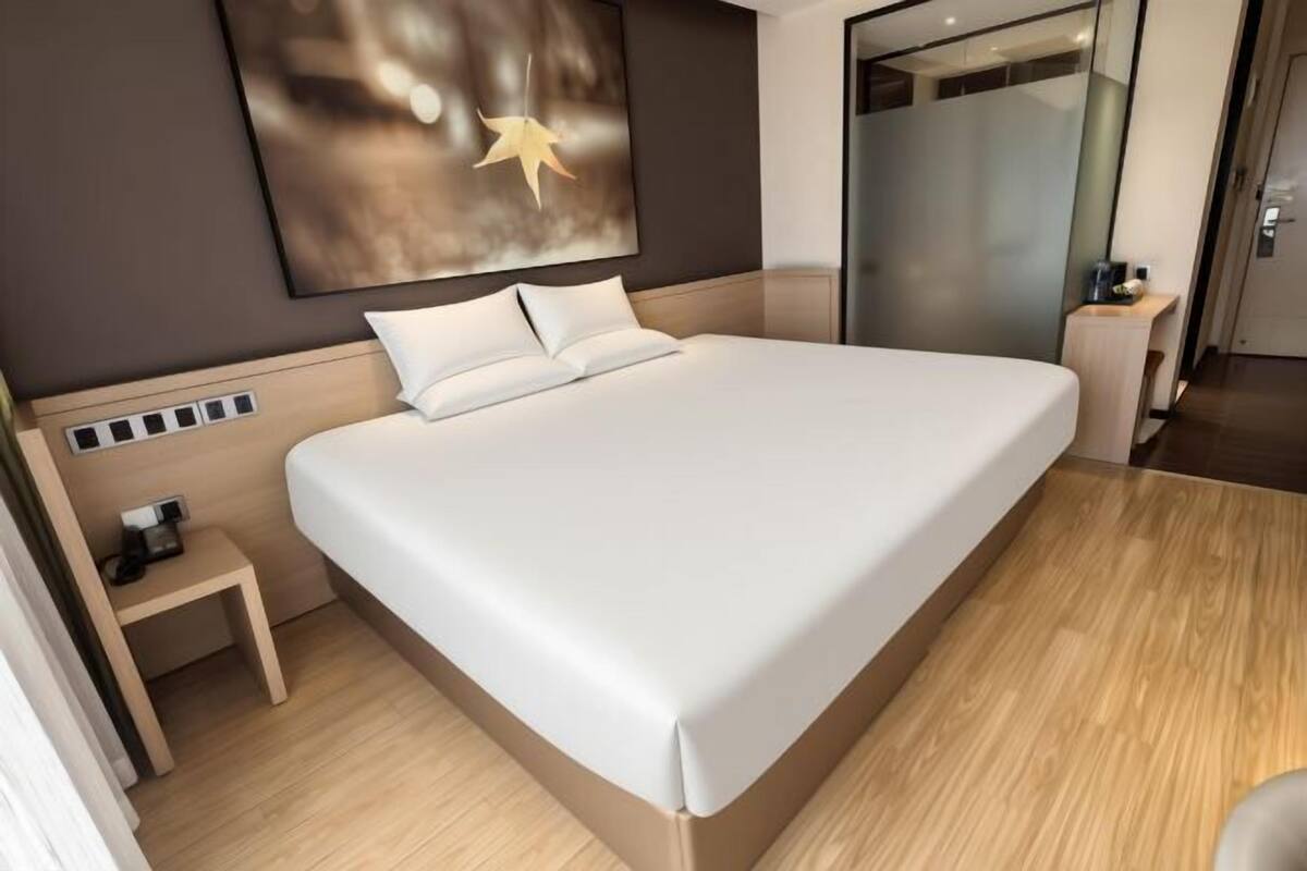 A modern hotel room with a large bed, a bedside table with a lamp, and a wall-mounted artwork.