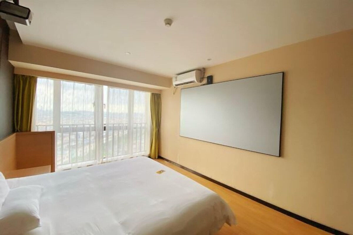 A hotel room with a large bed, a flat-screen TV mounted on the wall, and a window with curtains.