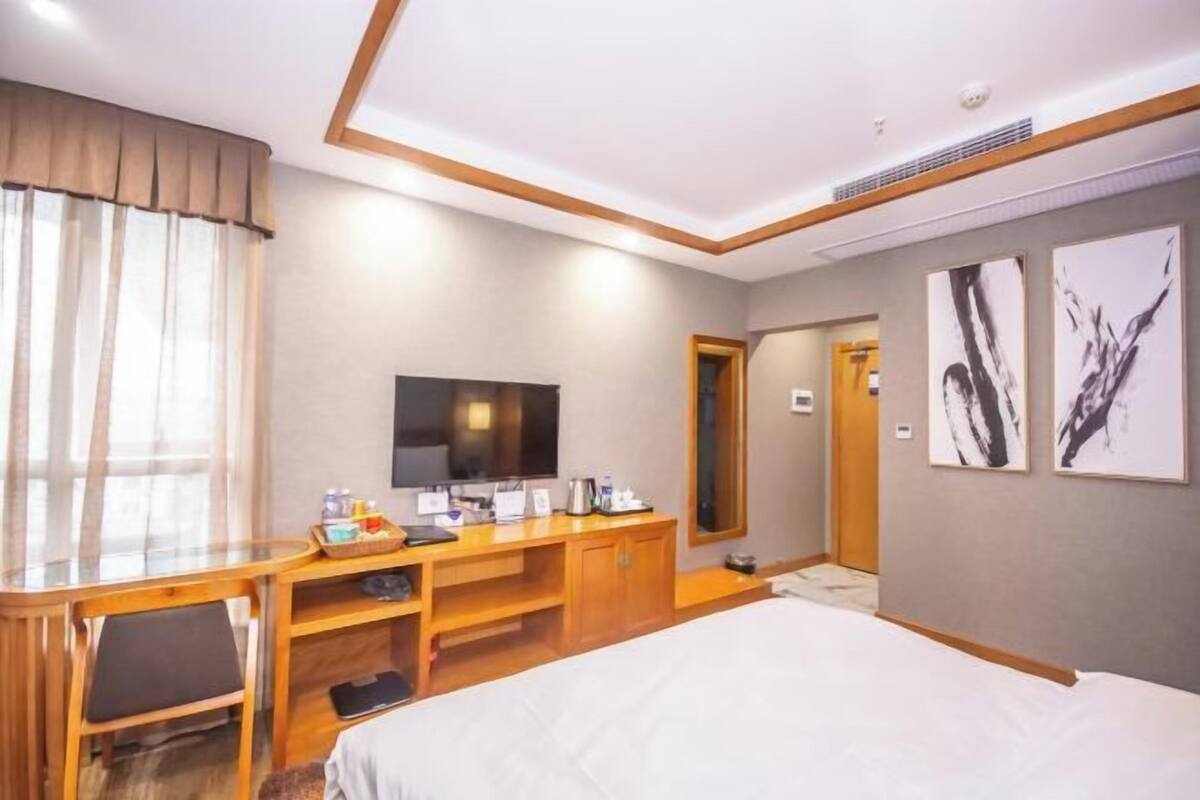 A hotel room with a bed, a desk with a flat-screen TV, a mirror, and artwork on the wall.